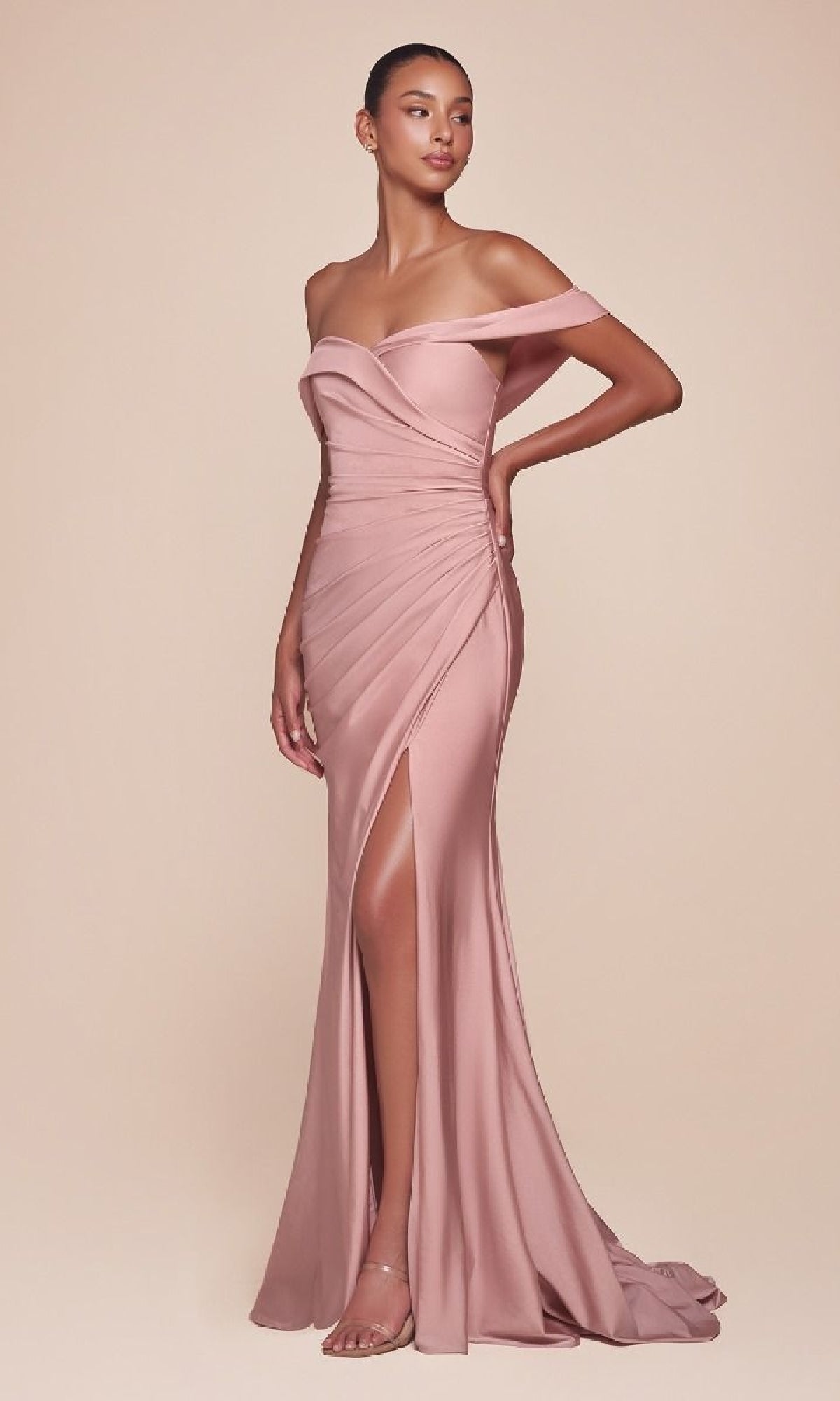 A woman poses in the Off-the-Shoulder Long Prom Dress: Ladivine CD790, a blush pink gown featuring a thigh-high slit and ruched detailing, styled with strappy heels against a plain beige background.